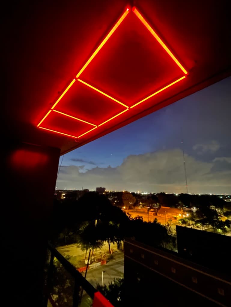 A red-lit GridLights ceiling grid on a Houston balcony at dusk, city skyline beyond.